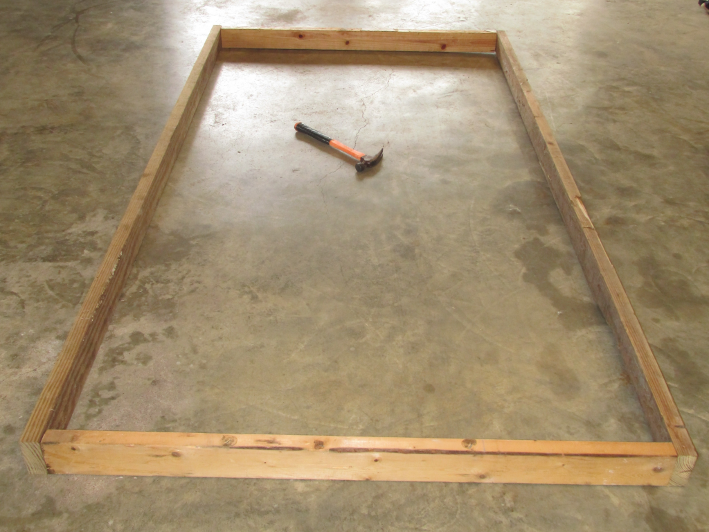 Rectangle chicken coop floor frame laying on concrete with hammer in center