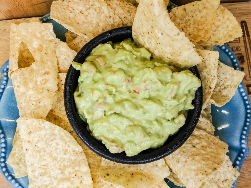 creamy bacon guacamole in a black bowl with tortilla chips around it 