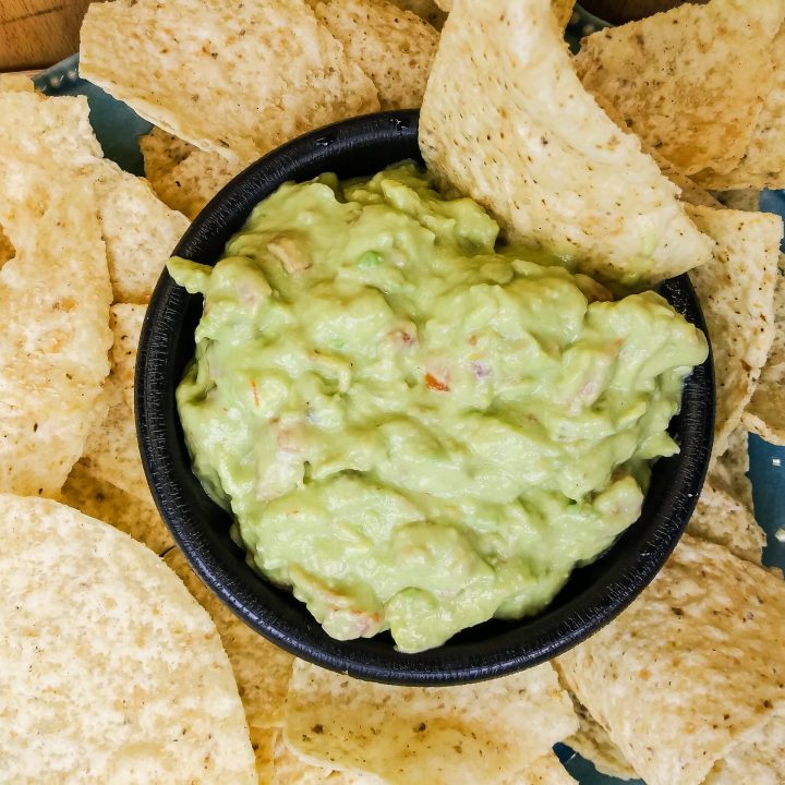 creamy bacon guacamole in a black bowl with tortilla chips around it