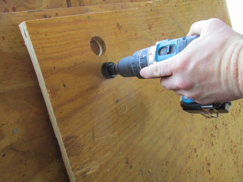 man's hand holding screw gun with hole saw attached cutting out circles in plywood